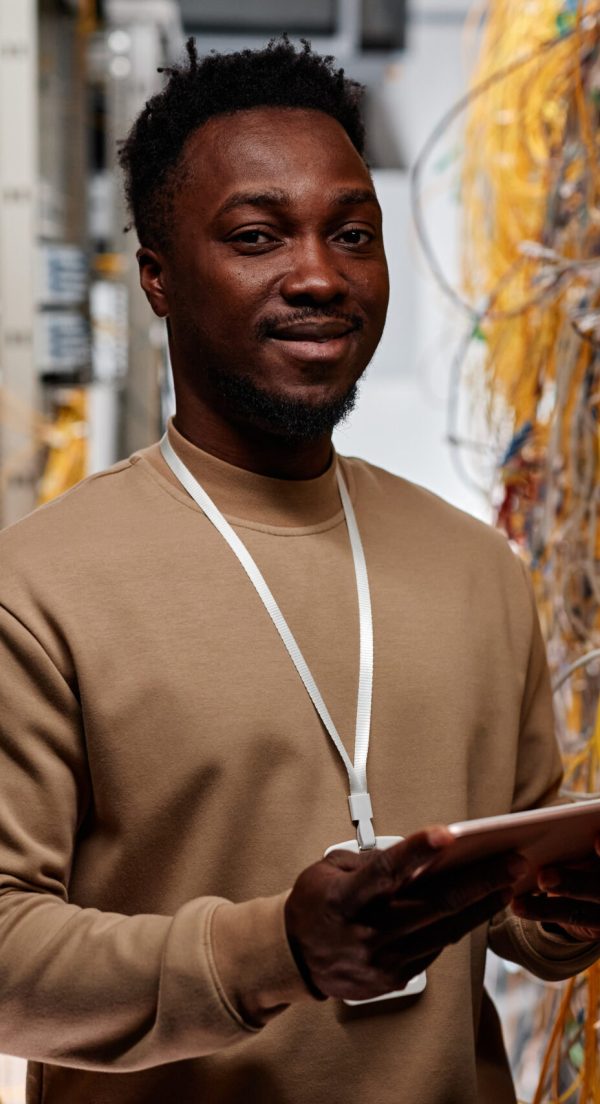 Waist up portrait of black man as system administrator standing in server room and smiling at camera